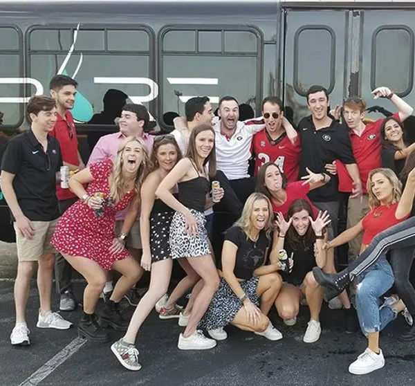 Game day group in red and white posing by a party bus